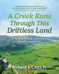 Book cover of 'A Creek Runs Through This Driftless Land' by Richard L. Cates Jr., featuring a scenic aerial view of a lush, green landscape with winding paths and a creek.