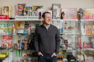 Sean Jacobsohn stands in front of a display case filled with novelty items and memorabilia, beneath a sign that reads 'FAILURE MUSEUM'.