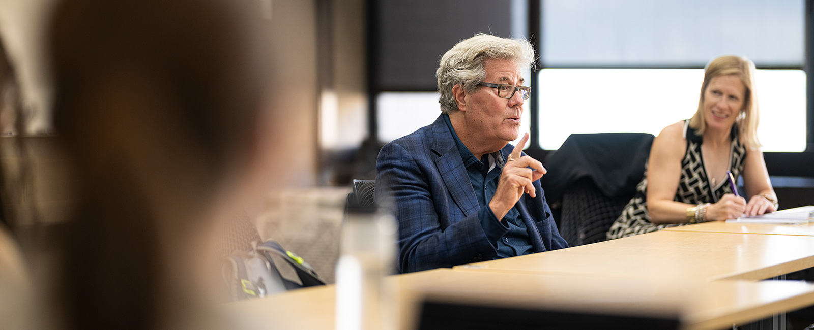 David Maraniss speaks in a classroom while a woman takes notes in the background.