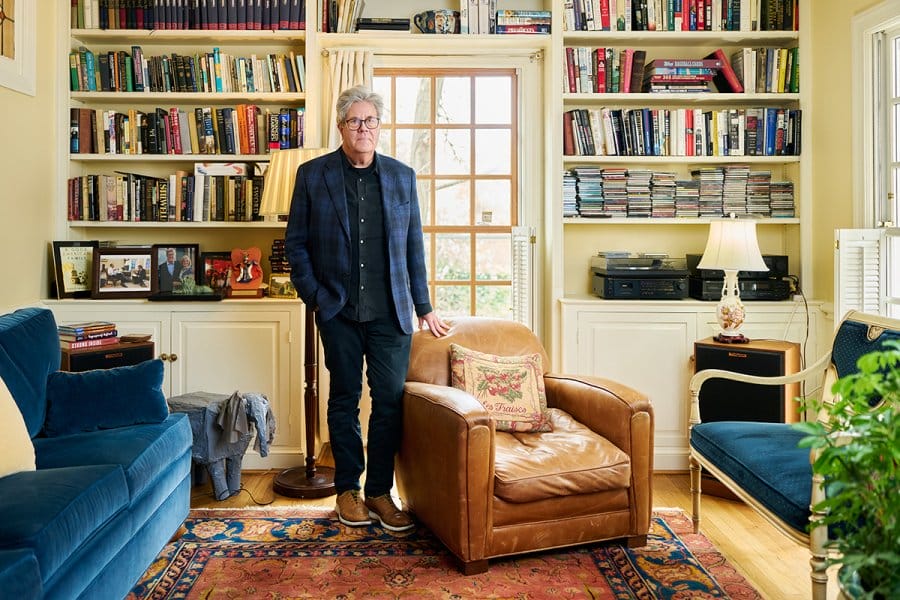 David Maraniss stands in a bright living room with bookshelves filled with books and CDs.