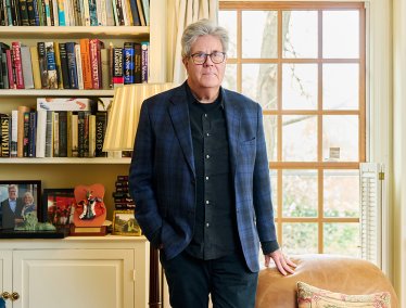 David Maraniss stands in a bright living room with bookshelves filled with books and CDs.