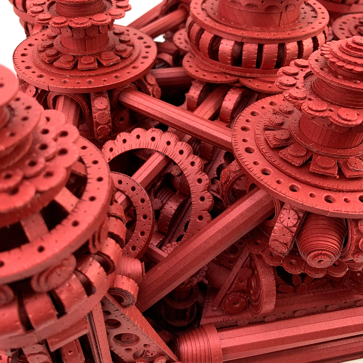 Close up of a highly detailed, intricate red paper sculpture resembling a complex mechanical structure with numerous gears, cogs, and symmetrical patterns.