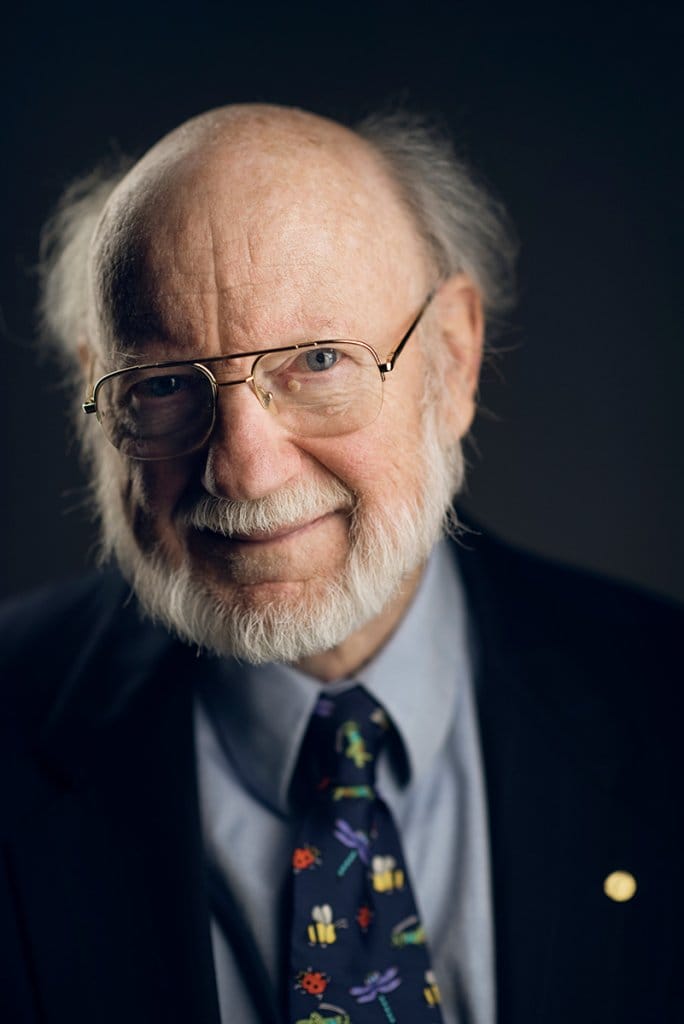 Headshot of William Campbell wearing glasses, a suit, and a tie with colorful insects on it.