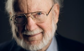 Headshot of William Campbell wearing glasses, a suit, and a tie with colorful insects on it.