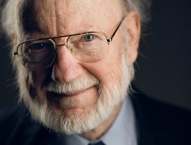 Headshot of William Campbell wearing glasses, a suit, and a tie with colorful insects on it.