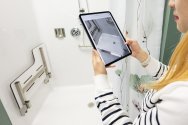 Grad student Dowon Lee demonstrates an app on an ipad in front of a shower stall