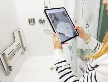 Grad student Dowon Lee demonstrates an app on an ipad in front of a shower stall