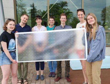 A group of smiling students pose holding a bird-safe window cover