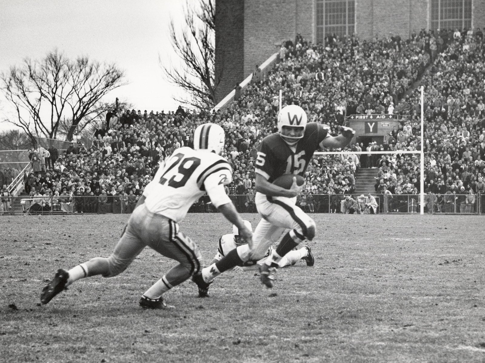 A black and white photo captures a football game moment as a Badger runs with the ball while a Gopher attempts a tackle, with a crowd of spectators in the background.