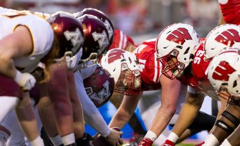 The Badger and Gopher football teams line up at the line of scrimmage, crouched and ready for the snap.