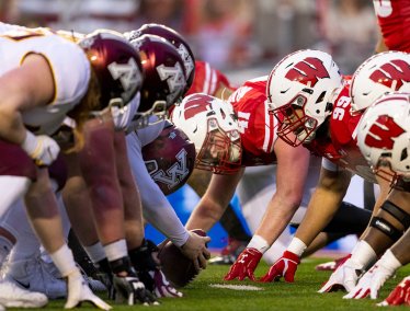 The Badger and Gopher football teams line up at the line of scrimmage, crouched and ready for the snap.