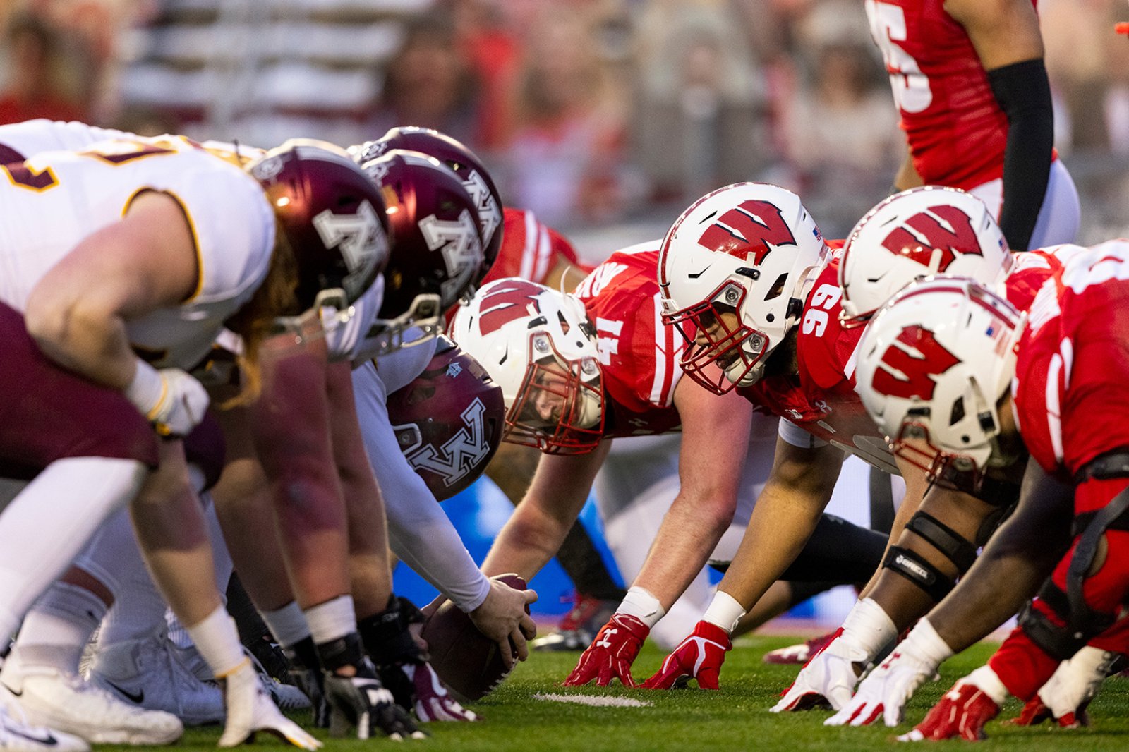 The Badger and Gopher football teams line up at the line of scrimmage, crouched and ready for the snap.