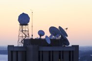 The rising sun silhouettes weather-related satellite dishes and a dome-shaped satellite-tracking antenna atop the Atmospheric, Oceanic, and Space Sciences Building
