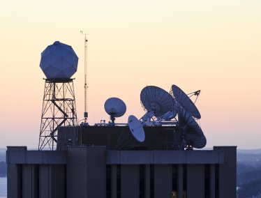 The rising sun silhouettes weather-related satellite dishes and a dome-shaped satellite-tracking antenna atop the Atmospheric, Oceanic, and Space Sciences Building