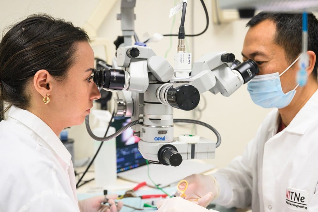 Two researchers in white lab coats work with a high-precision microscope equipped with a camera in a laboratory, highlighting advanced scientific research and technical expertise.