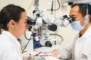 Two researchers in white lab coats work with a high-precision microscope equipped with a camera in a laboratory, highlighting advanced scientific research and technical expertise.