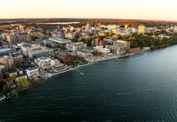 Aerial view of a the UW-Madison campus with numerous buildings, green spaces, and a waterfront.