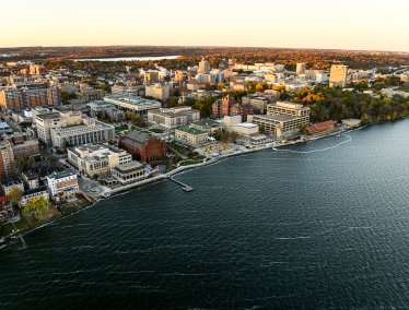 Aerial view of a the UW-Madison campus with numerous buildings, green spaces, and a waterfront.