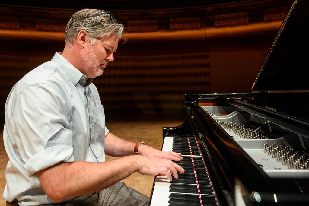 Dan Cavanagh plays a grand piano on a stage with a focused expression.