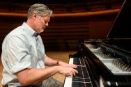 Dan Cavanagh plays a grand piano on a stage with a focused expression.