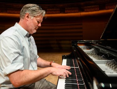 Dan Cavanagh plays a grand piano on a stage with a focused expression.