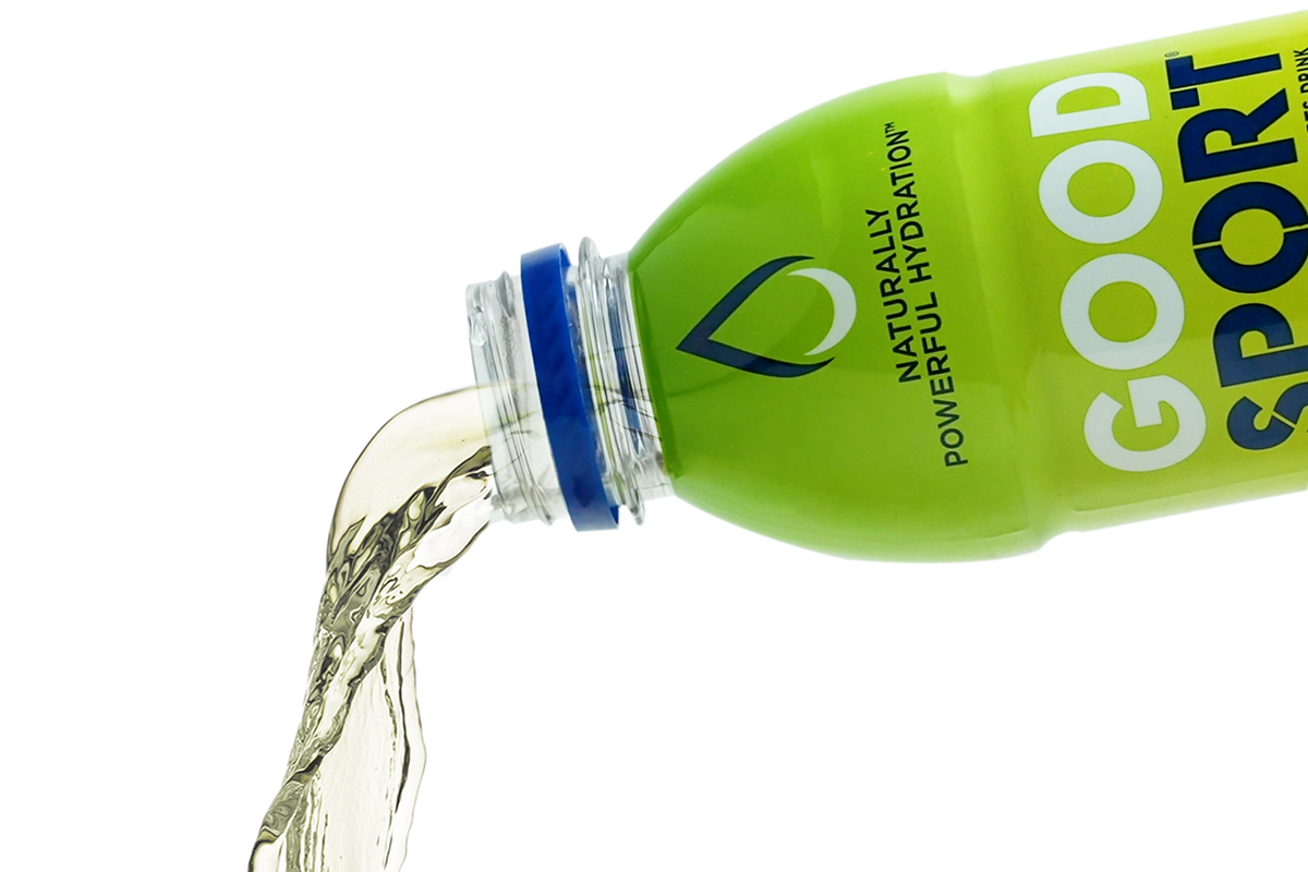A green bottle labeled 'GOOD SPORT' with the phrase 'NATURALLY POWERFUL HYDRATION' is tilted, pouring clear liquid.