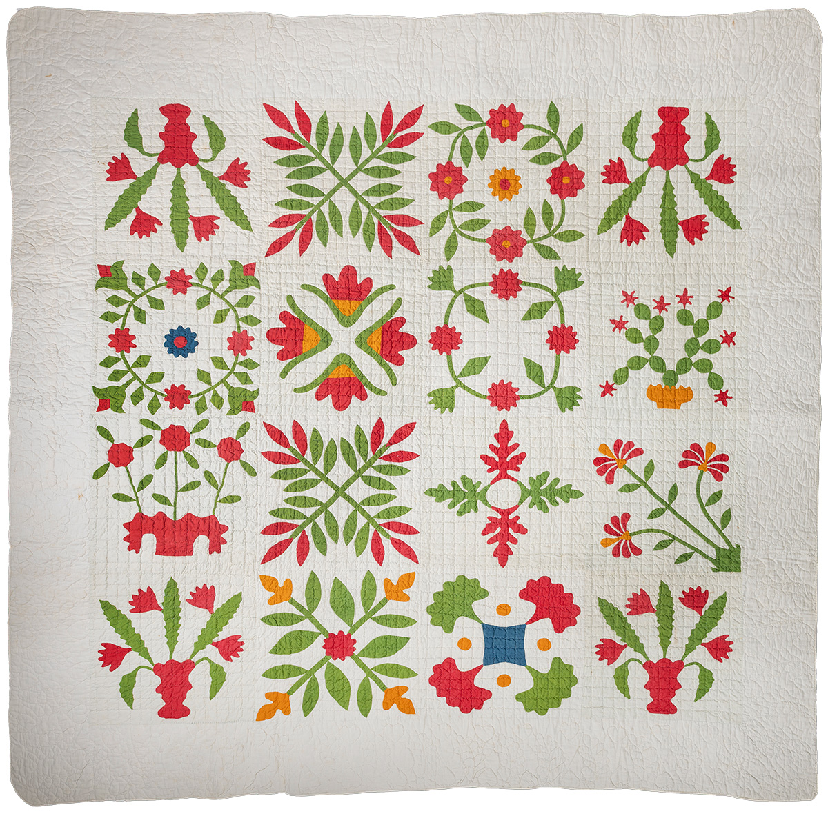 A white quilt decorated with floral and botanical applique designs in red, green, yellow, and orange.