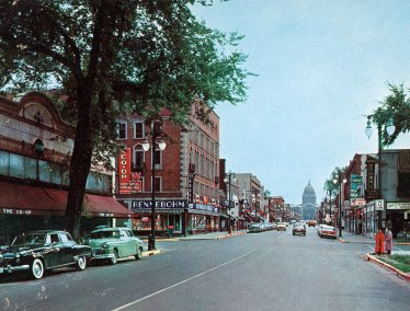 A vintage street scene of State Street with storefronts including 'Rennebohm' and the state capitol building in the background.