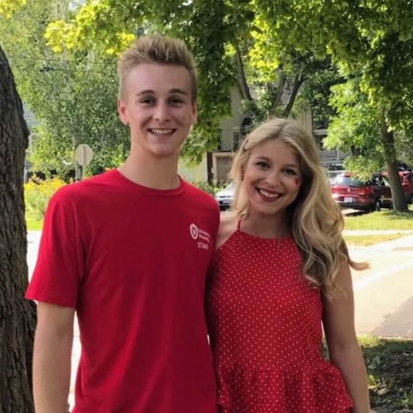 Two people stand outdoors on a sunny day, both wearing red clothing.