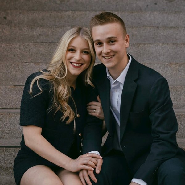 A couple sits close together on stone steps holding hands.