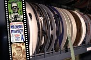 A shelf filled with colorful archival film reels, some with hanging strips.