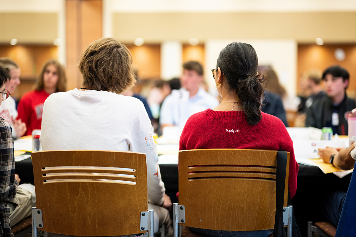 People sit at a round table in a bright, busy meeting room, participating in a group discussion.