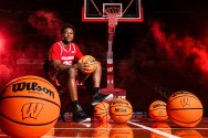 John Blackwell in a red uniform sits on a basketball court surrounded by several basketballs, with dramatic red lighting and smoke effects framing the hoop behind him.