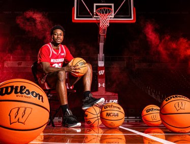 John Blackwell in a red uniform sits on a basketball court surrounded by several basketballs, with dramatic red lighting and smoke effects framing the hoop behind him.