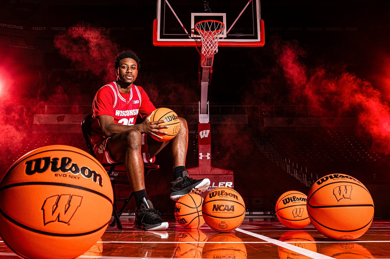 John Blackwell in a red uniform sits on a basketball court surrounded by several basketballs, with dramatic red lighting and smoke effects framing the hoop behind him.