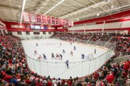 A packed arena watches as two hockey teams face off at center ice inside a brightly lit rink surrounded by cheering fans.