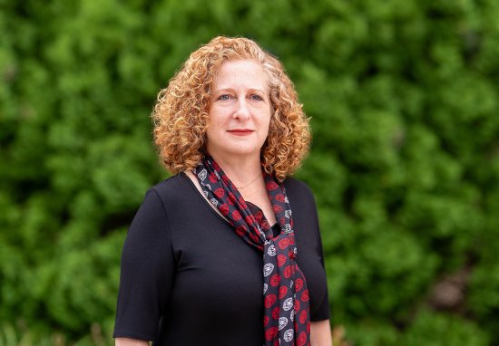 Chancellor Mnookin poses outdoors in front of a lush green background, wearing a dark top and a patterned scarf.
