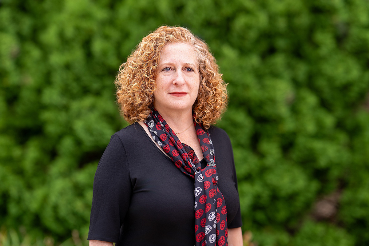 Chancellor Mnookin poses outdoors in front of a lush green background, wearing a dark top and a patterned scarf.