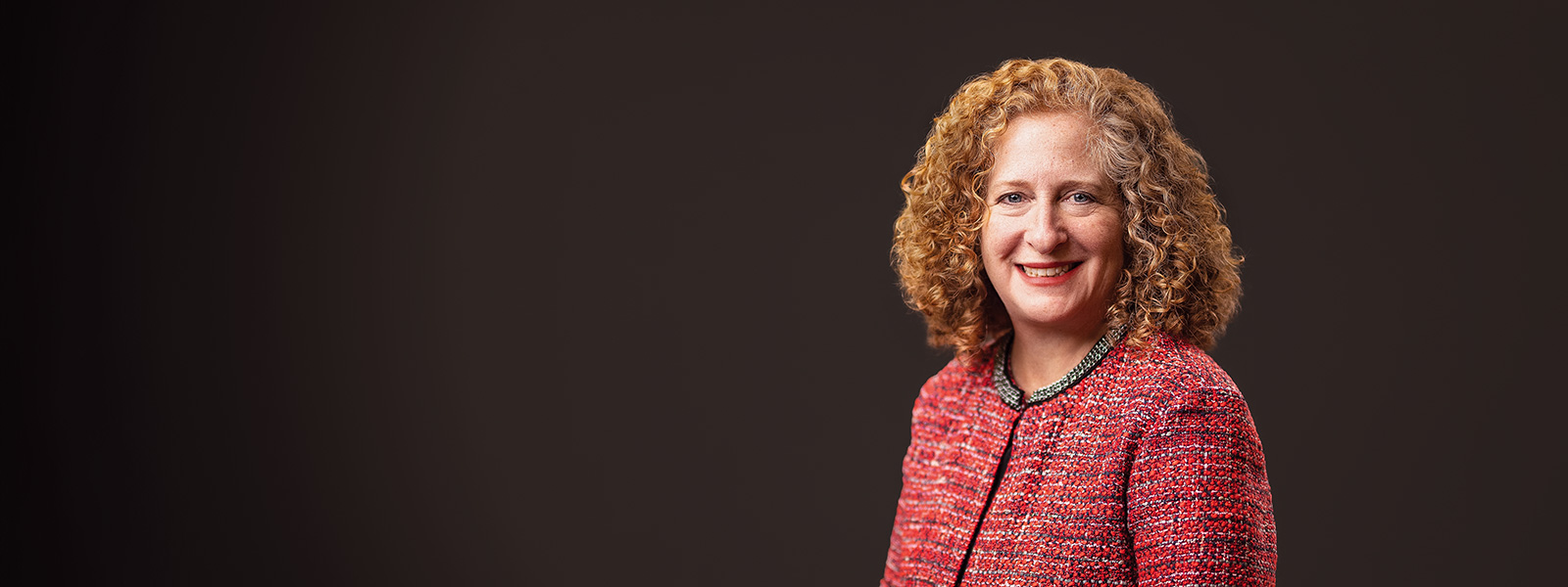 Chancellor Jennifer Mnookin wearing a textured red jacket against a dark background.