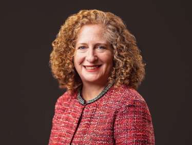 Chancellor Jennifer Mnookin wearing a textured red jacket against a dark background.
