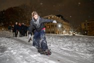 A female, smiling, snowboards down a snowy Bascom Hill at night while a group of people watch.