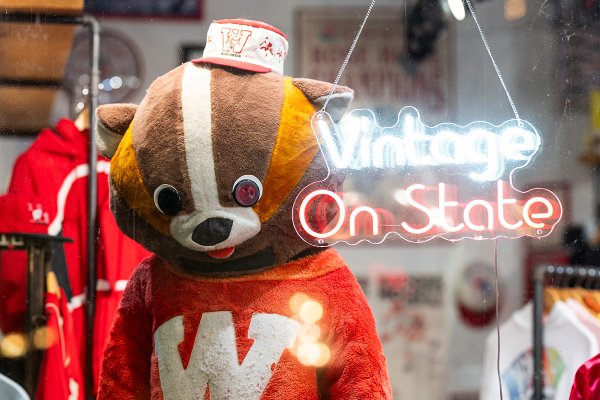A vintage-style badger mascot costume stands in a shop display next to a glowing neon sign reading 'Vintage On State'.