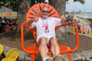 Todd Miller, wearing a white T‑shirt and marathon finisher medal, sits in a large orange terrace chair at the Memorial Union Terrace, giving two thumbs up.