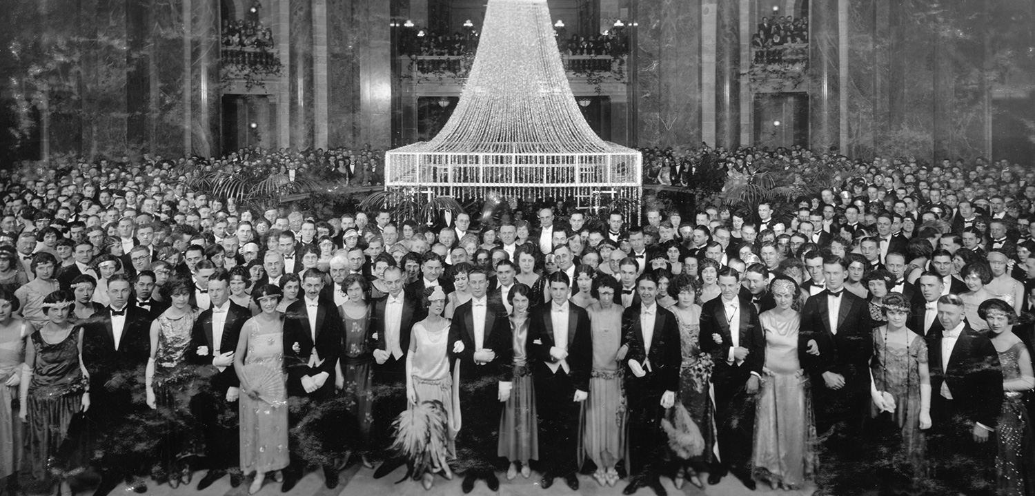 Black and white archival photo of a large crowd of elegantly dressed people poses in the Madison capitol building.