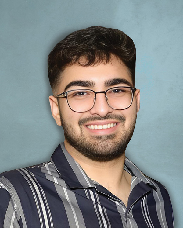 A portrait of a smiling young man with dark hair, a beard, and glasses, wearing a gray and black striped button-down shirt against a light blue textured background.