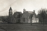A historic, sepia-toned photograph from 1890 showing the exterior of a large, stone music hall building with a prominent clock tower and Gothic-style architecture, surrounded by bare trees and an open lawn.