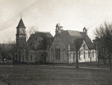 A historic, sepia-toned photograph from 1890 showing the exterior of a large, stone music hall building with a prominent clock tower and Gothic-style architecture, surrounded by bare trees and an open lawn.