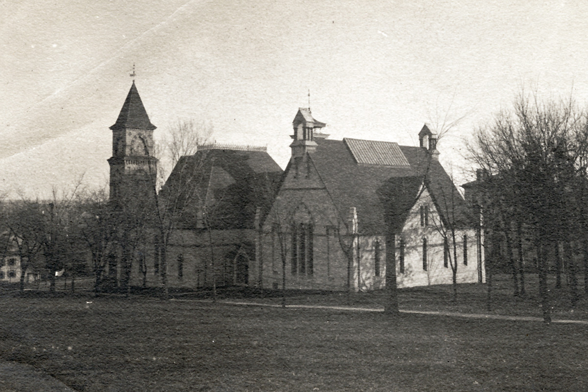 A historic, sepia-toned photograph from 1890 showing the exterior of a large, stone music hall building with a prominent clock tower and Gothic-style architecture, surrounded by bare trees and an open lawn.