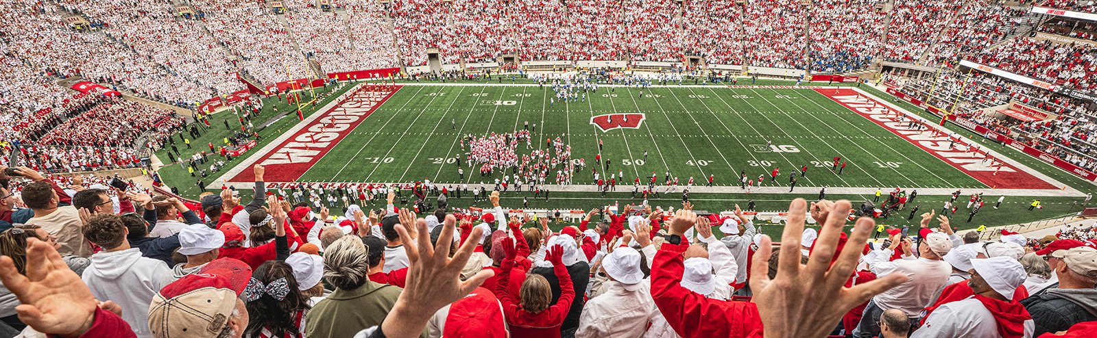 Fans in a packed stadium raise their hands in celebration while viewing a Badger football game at Camp Randall Stadium.