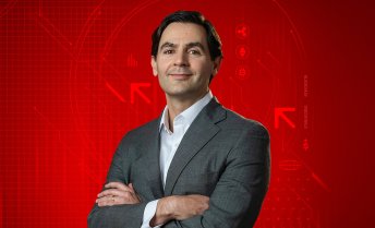 Portrait of Brad Chandler posing with crossed arms against a red graphic background featuring cryptocurrency logos and blockchain graphics.